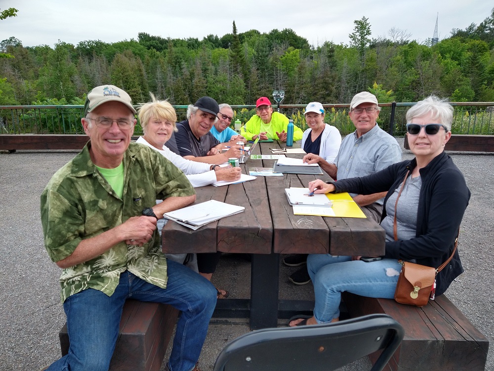 OVCATA volunteers Bob Peltzer, Pat Krose, Andy Kalnins, Larry Warden, Ish Theilheimer, Debbie Fiebig, Ron Moss and Debbie Macdonald discussing their Bike Bank at McRae Park in Eganville.